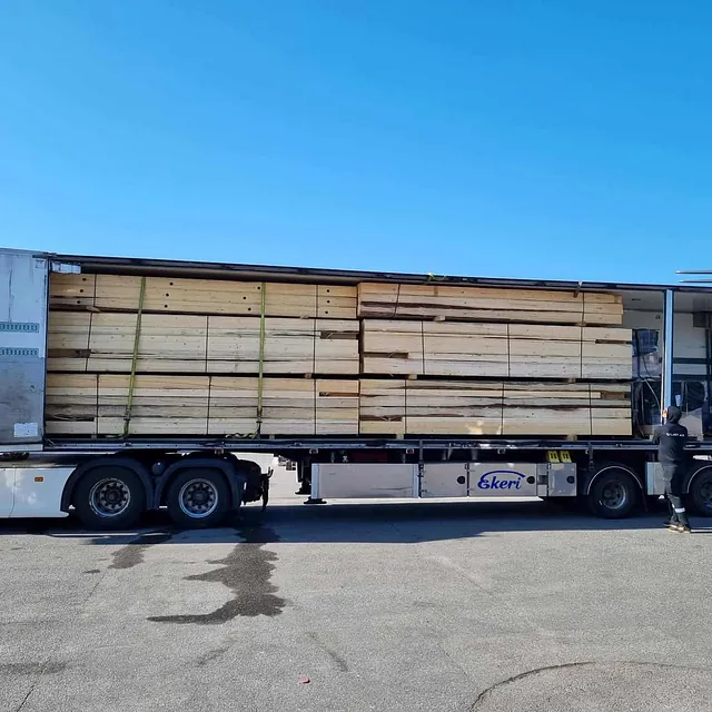 Lastebil lastet med stabile stabler av trevirke står parkert på industriområde.
